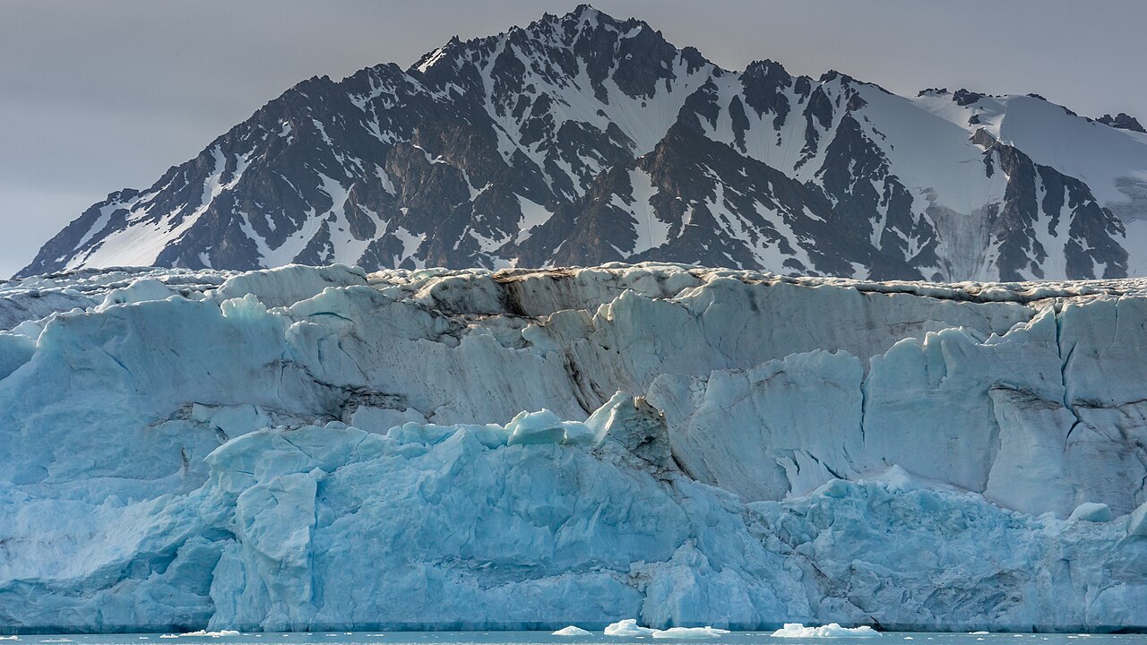 Front du glacier Raudfjordbreen au Svalbard, face à une étendue d’eau, avec reliefs enneigés à l’arrière-plan.